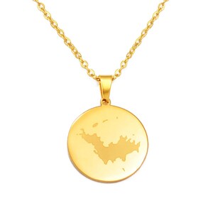 Puede incluir: Un collar de tono dorado con un colgante circular de superficie lisa y pulida. El centro del colgante muestra una silueta mate grabada con la forma de una masa terrestre o isla. El colgante cuelga de una delicada cadena dorada.