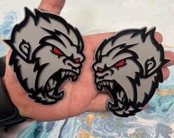 May include: Two gray and black gorilla head decals with red eyes and a snarling expression. The decals are on a hand.