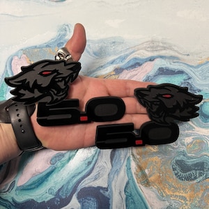 May include: Two black and red 5.0 emblems with a black wolf head design. The emblems are made of a durable material and are perfect for adding a touch of style to your car.
