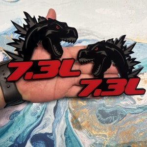May include: Two black dinosaur-shaped decals with red "7.3L" text. The decals are held in a hand.