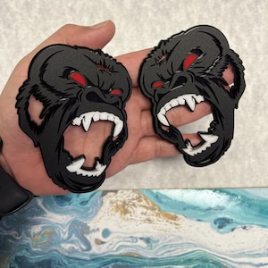May include: Two black gorilla head sculptures with red eyes and white teeth. The sculptures are made of a hard material and have a 3D effect.