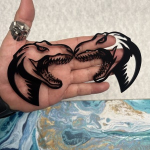 May include: Two black vinyl decals of a dinosaur head with a sharp, toothy grin. The decals are facing each other, creating a mirrored image.
