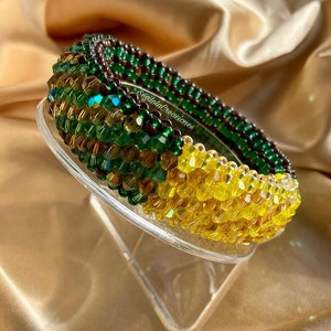 May include: A green and gold beaded bracelet with a brown beaded centre. The bracelet is made of small, faceted beads and is arranged in a spiral pattern.