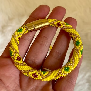 May include: A yellow beaded bracelet with red and green accents. The bracelet is made of small beads and has a magnetic clasp.