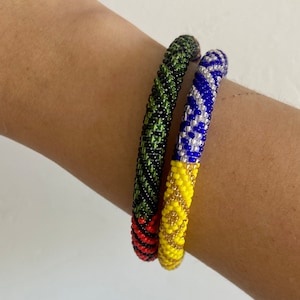 May include: Two beaded bracelets, one with black, green, and red beads, and the other with yellow, blue, and silver beads.