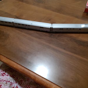 May include: A silver model train with two cars. The train is on a wooden surface.