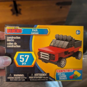 Könnte beinhalten: Eine rechteckige Schachtel für ein Make-It Blocks Bauset mit einem roten Lastwagen mit schwarzen Akzenten und vier Dachscheinwerfern. Die Verpackung zeigt den Text 57 pcs, truck, camion und weist auf die Kompatibilität mit führenden Marken hin.