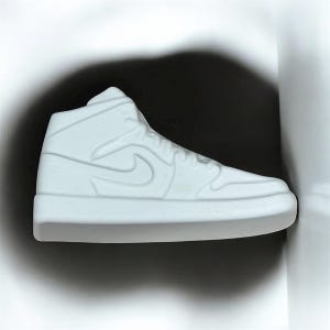 Op de afbeelding: Een witte high-top sneaker met een klassiek design, met het iconische swoosh-logo aan de zijkant. De schoen is uitgevoerd in effen, mat wit, met zichtbare stikdetails. De sneaker is een populaire stijl, vaak gedragen voor casual wear en sport.