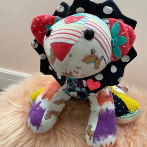 May include: A colorful patchwork lion stuffed animal with a black and white polka dot mane, rainbow and strawberry patterns, and a pink heart on its chest.