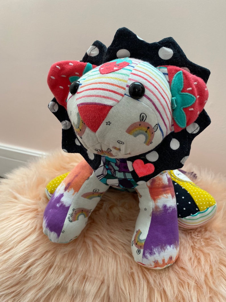 May include: A colorful patchwork lion stuffed animal with a black and white polka dot mane, rainbow and strawberry patterns, and a pink heart on its chest.