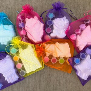 Puede incluir: Una colecci&oacute;n de kits para pintar con formas de gatos y edificios. Cada kit incluye una figura de yeso, botes de pintura y un pincel, todo empaquetado en bolsas de malla de colores con cierres de cord&oacute;n. Los kits son de varios colores.