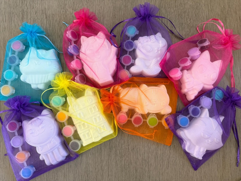 Puede incluir: Una colecci&oacute;n de kits para pintar con formas de gatos y edificios. Cada kit incluye una figura de yeso, botes de pintura y un pincel, todo empaquetado en bolsas de malla de colores con cierres de cord&oacute;n. Los kits son de varios colores.
