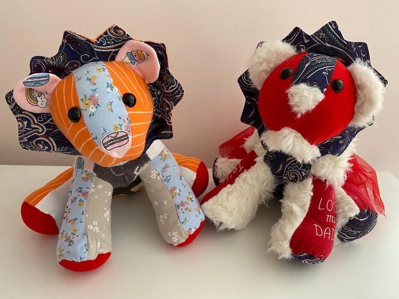 May include: Two handmade patchwork lion plushies. One is orange and blue with a rainbow and ice cream cone on its chest. The other is red with white fur and a blue and white paisley pattern. The red lion has the text "Love my Dad" embroidered on its leg.