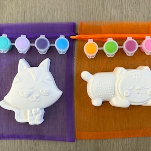 Puede incluir: Dos kits para pintar. Un kit presenta una figura de zorro blanco y un juego de pinturas turquesa, lila, morado y azul. El otro kit incluye una figura de gato blanco y un juego de pinturas amarillas, verdes, magenta y rosas. Ambos kits est&aacute;n en bolsas de malla.