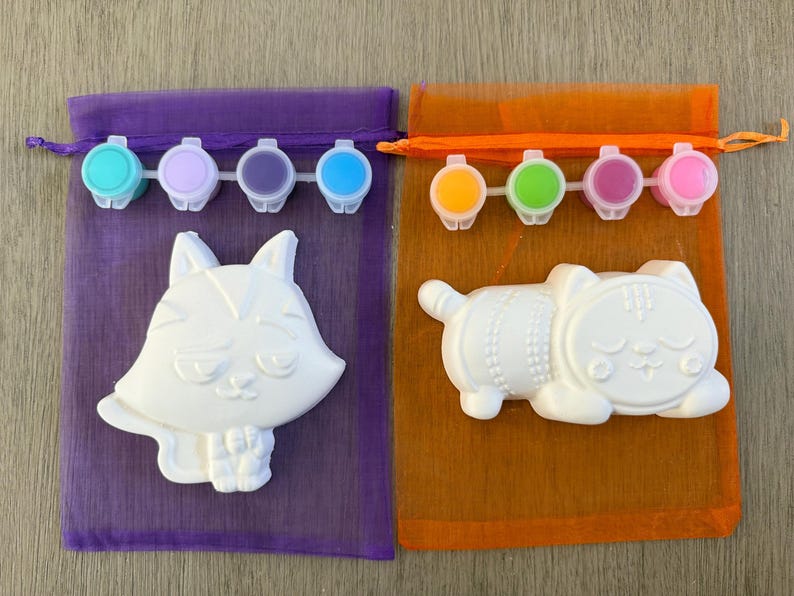 Puede incluir: Dos kits para pintar. Un kit presenta una figura de zorro blanco y un juego de pinturas turquesa, lila, morado y azul. El otro kit incluye una figura de gato blanco y un juego de pinturas amarillas, verdes, magenta y rosas. Ambos kits est&aacute;n en bolsas de malla.