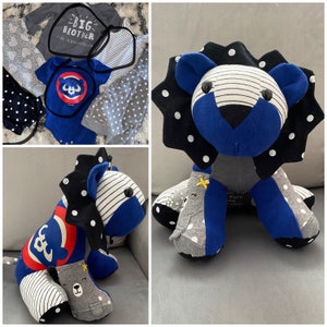 May include: A handmade stuffed lion toy made from repurposed baby clothes. The lion is blue, black, and white with a gray and white polka dot pattern. The lion has a black nose and black eyes. The lion is sitting on a white surface.