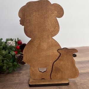 Puede incluir: Silueta de madera de una persona con un saco. La figura es de color marr&oacute;n claro con un contorno detallado. La base es de color marr&oacute;n m&aacute;s oscuro, proporcionando estabilidad. El dise&ntilde;o es sencillo y r&uacute;stico, adecuado para decoraciones festivas.