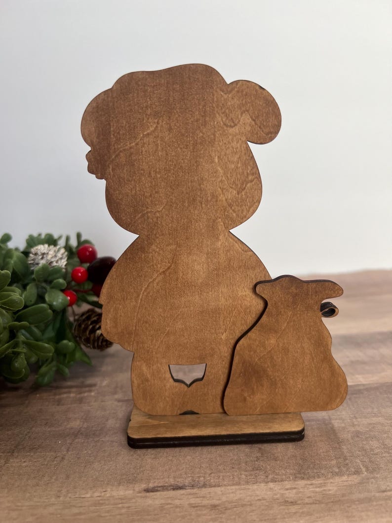 Puede incluir: Silueta de madera de una persona con un saco. La figura es de color marr&oacute;n claro con un contorno detallado. La base es de color marr&oacute;n m&aacute;s oscuro, proporcionando estabilidad. El dise&ntilde;o es sencillo y r&uacute;stico, adecuado para decoraciones festivas.