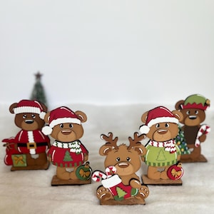Puede incluir: Un conjunto de figuras de osos navide&ntilde;os de madera. Cada oso viste atuendos festivos, incluyendo gorros de Pap&aacute; Noel y su&eacute;teres. Algunos osos sostienen bastones de caramelo o adornos, creando una alegre exhibici&oacute;n navide&ntilde;a.