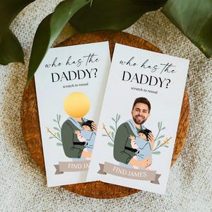 Puede incluir: Dos tarjetas blancas con una ilustración azul y verde de una persona sosteniendo un bebé. El texto en las tarjetas dice "who has the DADDY?" y "scratch to reveal". Una tarjeta tiene un círculo dorado que cubre la cara de la persona, la otra tarjeta muestra la cara de un hombre. La parte inferior de las tarjetas dice "FIND JA" y "FIND JAMES".