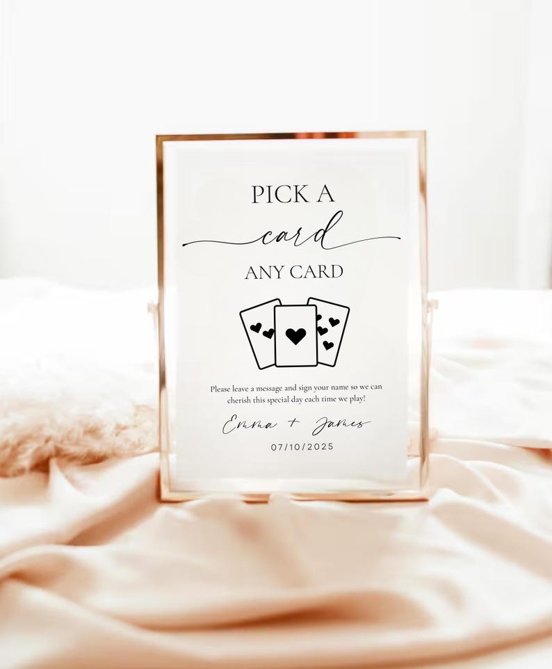 以下が含まれることがあります： 「PICK A card ANY CARD」という文字と、ハートのマークが描かれたトランプ4枚のグラフィックが書かれた、金色の枠のある白い看板。看板には、「Please leave a message and sign your name so we can cherish this special day each time we play! Emma + James 07/10/2025」という文字も書かれている。