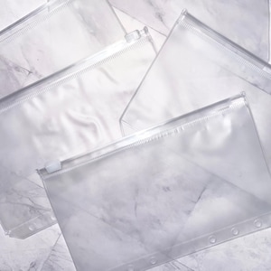 Peut inclure: Plusieurs pochettes transparentes à fermeture éclair, parfaites pour organiser des documents ou de petits objets. Les pochettes sont transparentes, permettant de voir le contenu. Fermeture éclair et bords renforcés. Fond marbré gris clair.