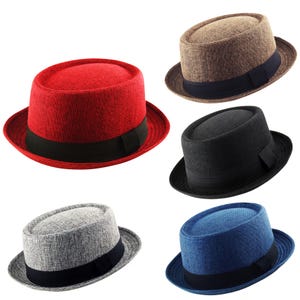 Puede incluir: Colección de cinco sombreros fedora en varios colores: rojo, marrón, negro, gris y azul. Cada sombrero tiene una banda negra alrededor de la corona y un ala corta. Los sombreros están hechos de tela texturizada.