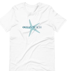 Peut inclure: T-shirt blanc avec une étoile de mer bleue et le texte "Ocean Beach" imprimé sur le devant.
