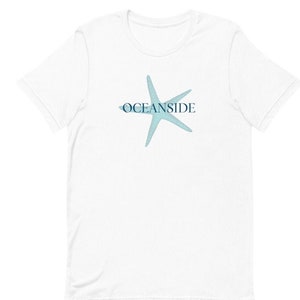 Peut inclure: T-shirt blanc avec une étoile de mer bleue et le texte "OCEANSIDE" imprimé sur le devant.