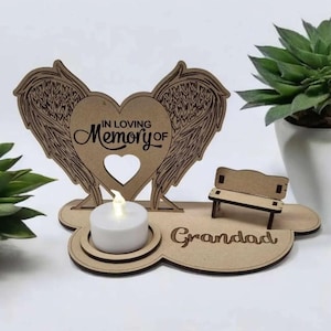 May include: A wooden memorial ornament featuring angel wings, a heart, and a miniature bench. The heart has a cutout and the words "IN LOVING Memory of" are inscribed. A small candle sits in front of the heart, with "Grandad" at the base.