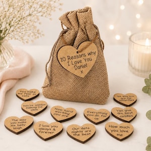 May include: A tan hessian drawstring pouch with a wooden heart tag inscribed with 10 Reasons why I Love You Daniel X. Ten smaller wooden hearts are arranged in front, each engraved with phrases such as You make me feel so safe and I love you always & forever.