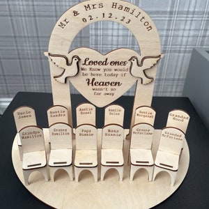 May include: Wooden memorial with a heart-shaped archway and doves, inscribed with "Loved ones, We know you would be here today if Heaven wasn't so far away."  Below the archway are ten small wooden chairs with names inscribed on each chair.
