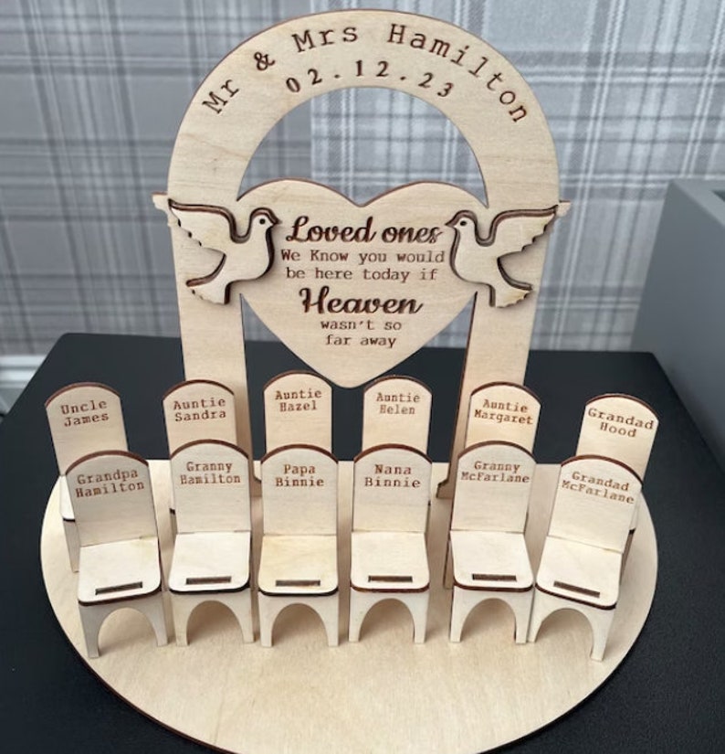 May include: Wooden memorial with a heart-shaped archway and doves, inscribed with "Loved ones, We know you would be here today if Heaven wasn't so far away."  Below the archway are ten small wooden chairs with names inscribed on each chair.