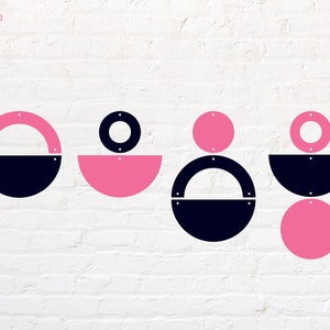 May include: A set of nine geometric shapes in pink and black. The shapes are circles, semi-circles, and rings. The shapes are arranged in a pattern on a white brick wall.