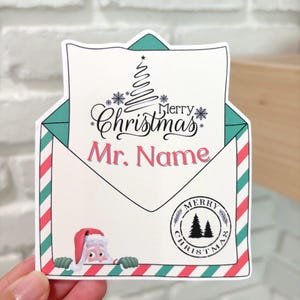 May include: A white envelope with a red and green striped border. The envelope has a green flap with a Christmas tree and the text "Merry Christmas" and "Mr. Name". A Santa Claus figure peeks out from behind the envelope. A green circle with the text "Merry Christmas" and a pine tree design is in the bottom right corner.