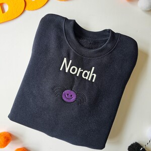 Black crew neck sweatshirt, embroidered with a purple spider and personalised with childs name in glow in the dark thread. Machine embroidered in the UK