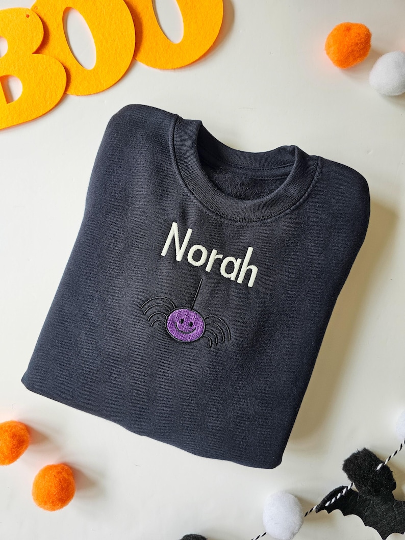 Black crew neck sweatshirt, embroidered with a purple spider and personalised with childs name in glow in the dark thread. Machine embroidered in the UK