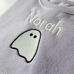 zoomed in image of lilac crew neck sweatshirt, embroidered with glow in the dark ghost personalised with childs name. Machine embroidered in the UK