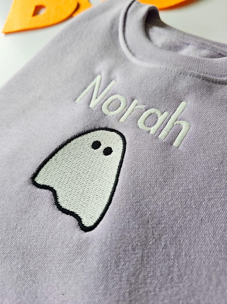 zoomed in image of lilac crew neck sweatshirt, embroidered with glow in the dark ghost personalised with childs name. Machine embroidered in the UK