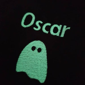 Zoomed in image of embroidered Glow in the dark ghost and personalised with childs name whilst glowing in the dark with a green glow. Machine embroidered in the UK