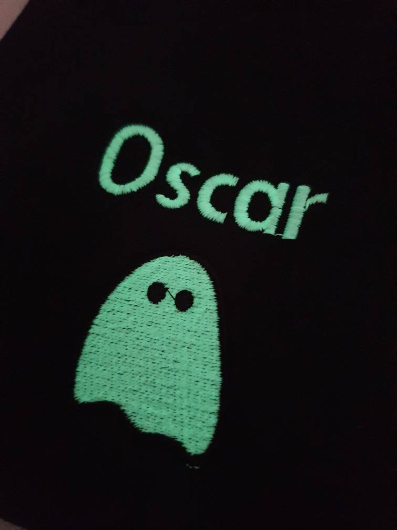 Zoomed in image of embroidered Glow in the dark ghost and personalised with childs name whilst glowing in the dark with a green glow. Machine embroidered in the UK
