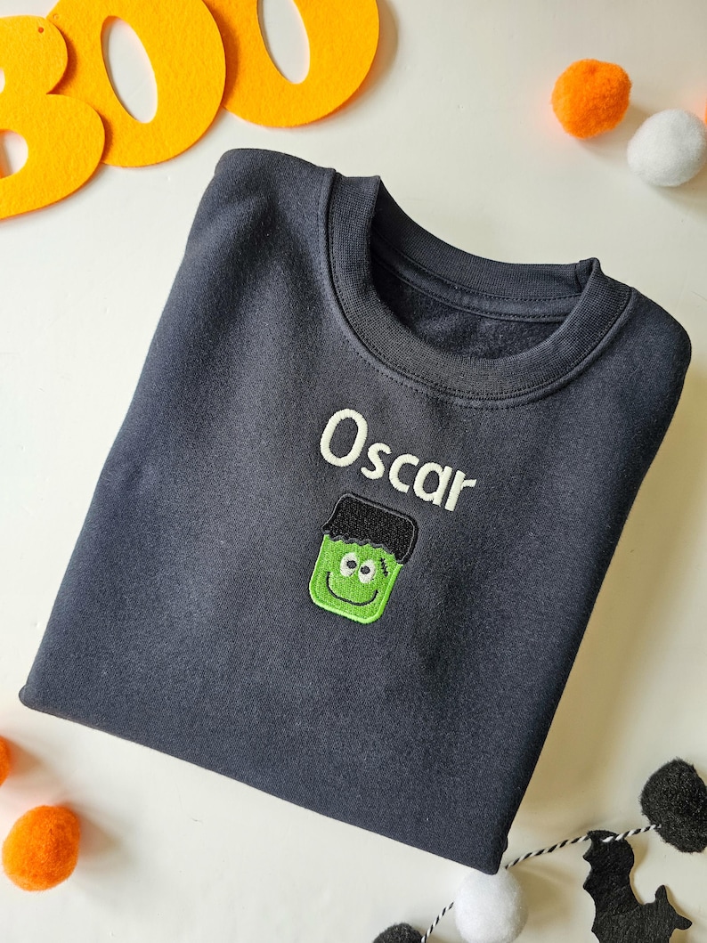 Black crew neck sweatshirt, embroidered with a green monster and personalised with childs name in glow in the dark thread. Machine embroidered in the UK