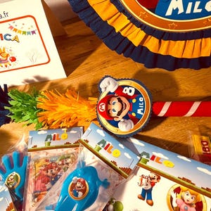 May include: A party favor set with a Mario theme. The set includes a pinata, a noisemaker, a party favor bag, and a small toy. The pinata is blue and yellow with a Mario character on it. The noisemaker is red and white with a Mario character on it. The party favor bag is blue and yellow with a Mario character on it. The small toy is a blue and yellow Mario character.