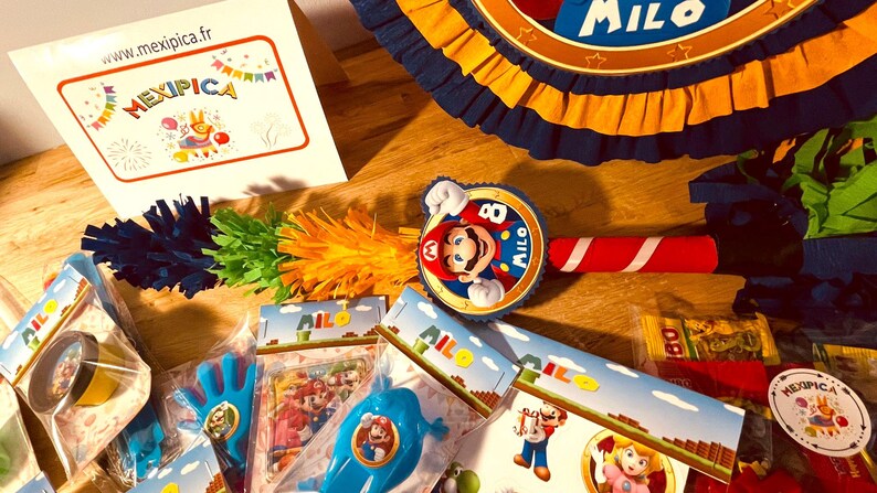 May include: A party favor set with a Mario theme. The set includes a pinata, a noisemaker, a party favor bag, and a small toy. The pinata is blue and yellow with a Mario character on it. The noisemaker is red and white with a Mario character on it. The party favor bag is blue and yellow with a Mario character on it. The small toy is a blue and yellow Mario character.