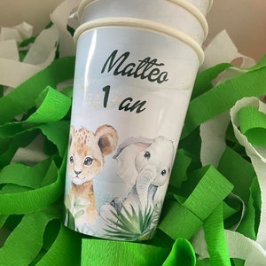 Może przedstawiać: Stos niebieskich papierowych kubków z motywem lwa i słonia. Górny kubek ma napis Matteo i cyfrę 1 z napisem "an" poniżej.