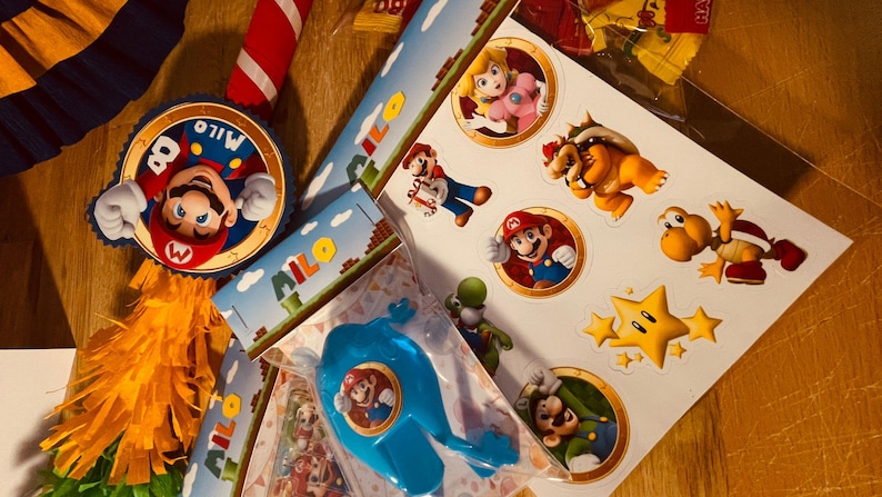 May include: A colorful Mario-themed party decoration set with a pinata, banners, and stickers. The pinata features a large image of Mario with the name "Milo" on it. The banners have the name "Milo" printed on them and feature a Mario-themed design. The stickers feature various characters from the Mario franchise, including Mario, Luigi, Bowser, and Toad.
