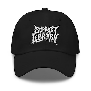May include: Black baseball cap with the white text "SUPPORT YOUR LOCAL LIBRARY" in a stylized font. The cap has a curved brim and an adjustable strap at the back. The hat is made of a soft, durable material.