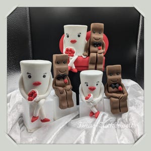 Könnte beinhalten: Ein Set aus fünf Fondantfiguren, darunter zwei Paare, die jeweils einen kleinen Strauß roter Blumen halten. Die Figuren sind so gestaltet, dass sie wie Schokoladentafeln und Tassen aussehen. Die Figuren sitzen auf weißen Tortenständern.