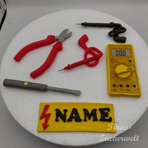 Könnte beinhalten: Ein gelber Kuchen, der mit roten und grauen Werkzeugen verziert ist, darunter eine Zange, ein Schraubendreher und ein Multimeter. Der Kuchen ist außerdem mit einem gelben Schild mit einem Blitz und dem Wort "NAME" verziert.