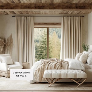 Op de afbeelding: Een slaapkamer met een bed met wit beddengoed en een beige deken. De kamer heeft beige gordijnen, een witte fauteuil en een bank. De tekst "Coconut White C1-VW-1" is zichtbaar.
